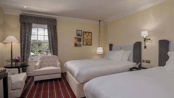 A hotel room with two beds, a chair, a table, a lamp, and a window with curtains.