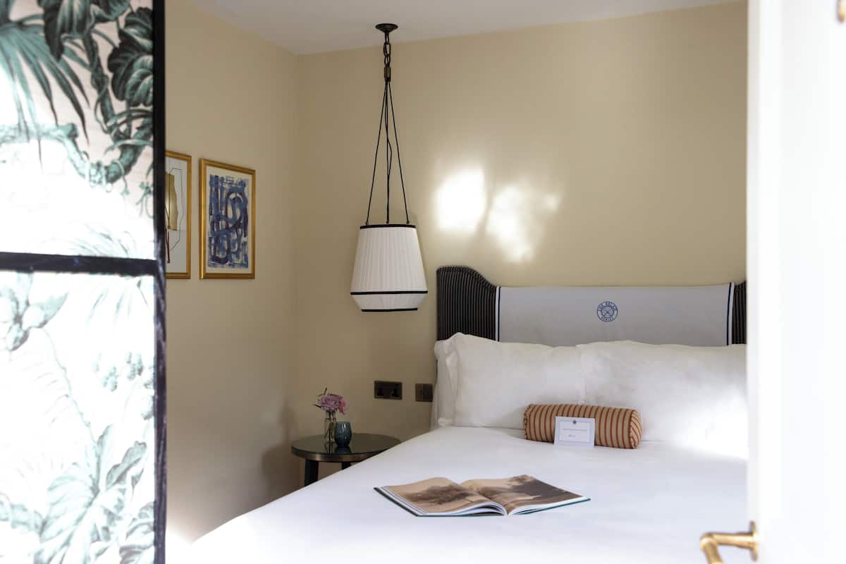 A hotel room with a bed, a nightstand, a lamp, and a framed picture on the wall.