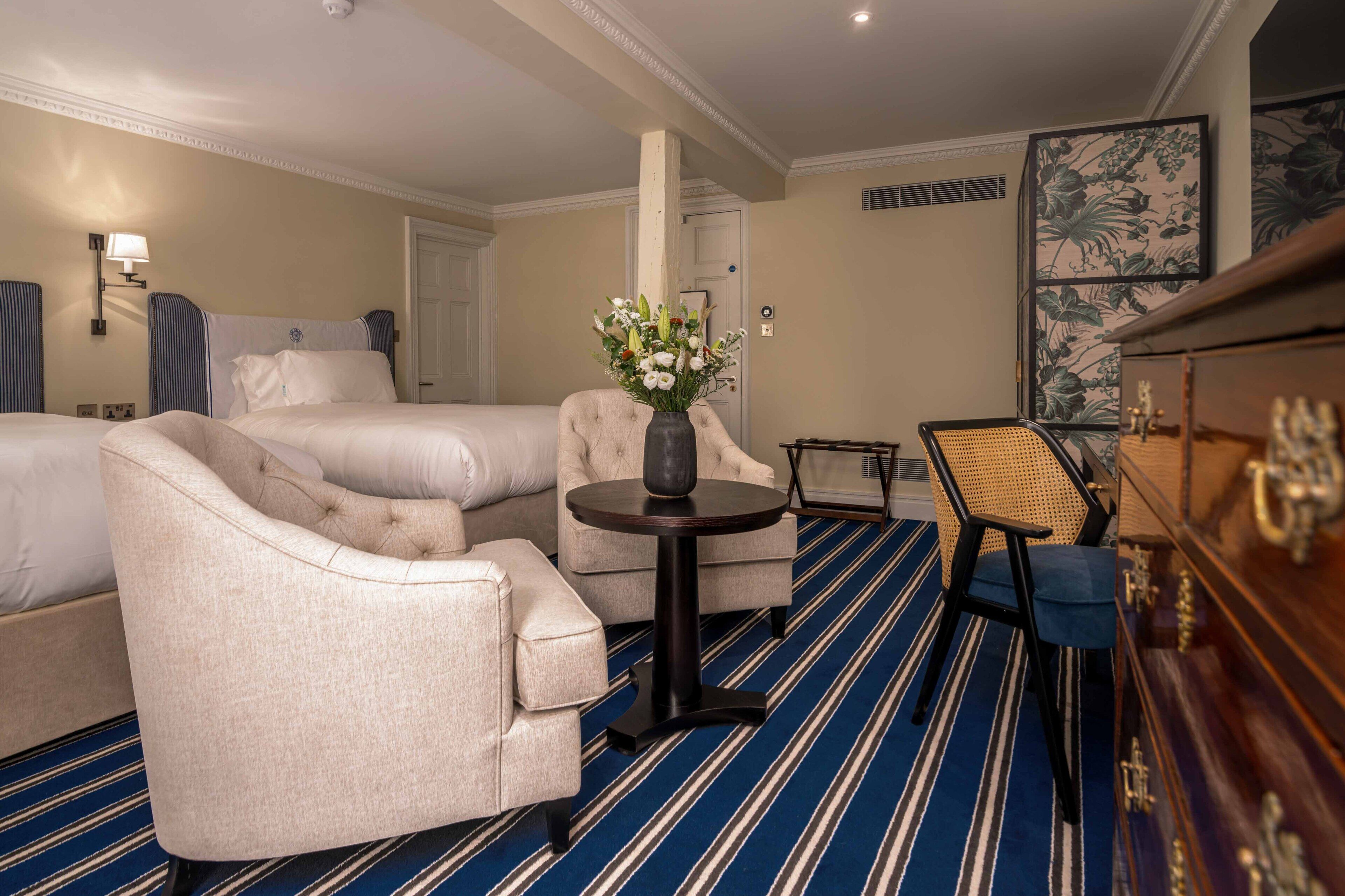 A hotel room with two beds, a sofa, a small round table with a vase of flowers, a chair, and a wooden cabinet.