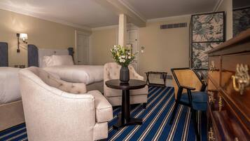A hotel room with two beds, a sofa, a small round table with a vase of flowers, a chair, and a wooden cabinet.