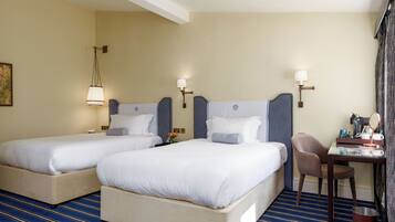 Habitación de hotel con dos camas, un escritorio con silla, y una mesita de noche con espejo y artículos de aseo.