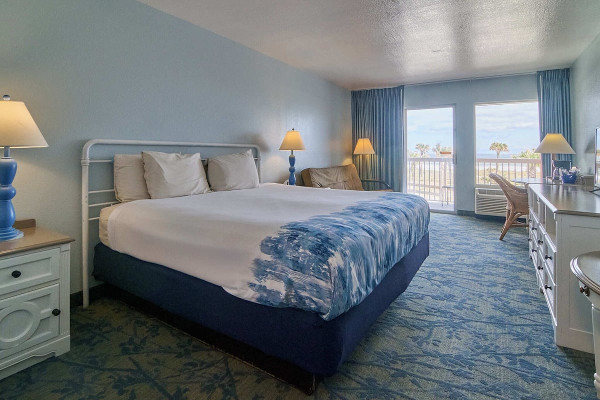 A hotel room with a bed, two bedside lamps, a dresser, and a view of the balcony.