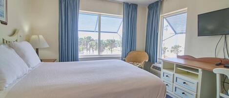A hotel room with a large bed, a desk with drawers, a chair, a TV, and a window with curtains.