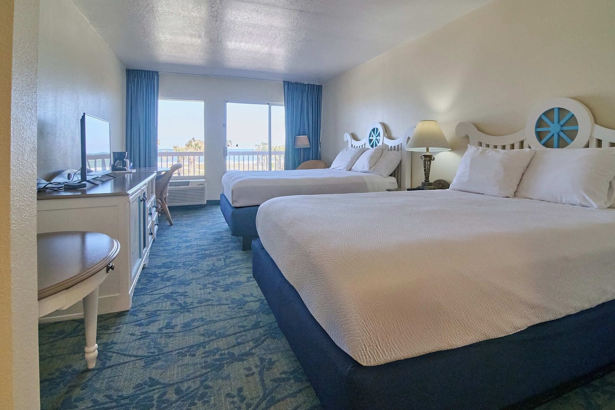 A hotel room with two beds, a desk, and a chair.