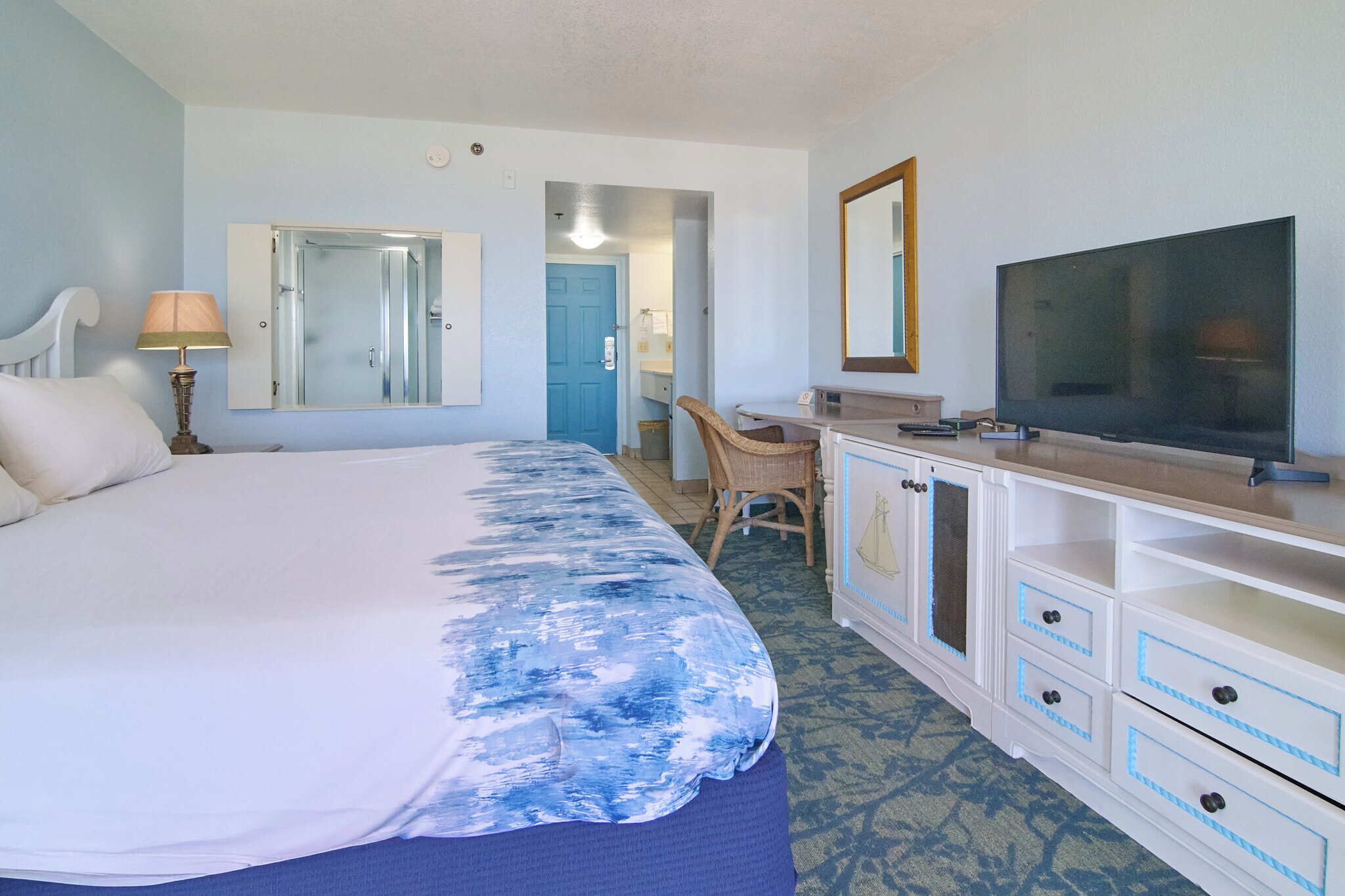 Habitación de hotel con cama, escritorio, televisor y espejo.