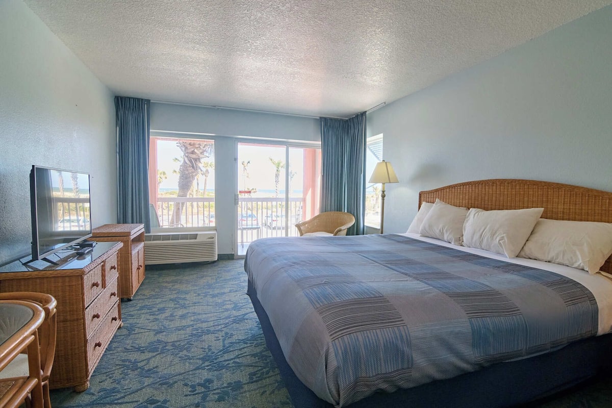 A hotel room with a large bed, a television, a desk, and a view of the outdoors.