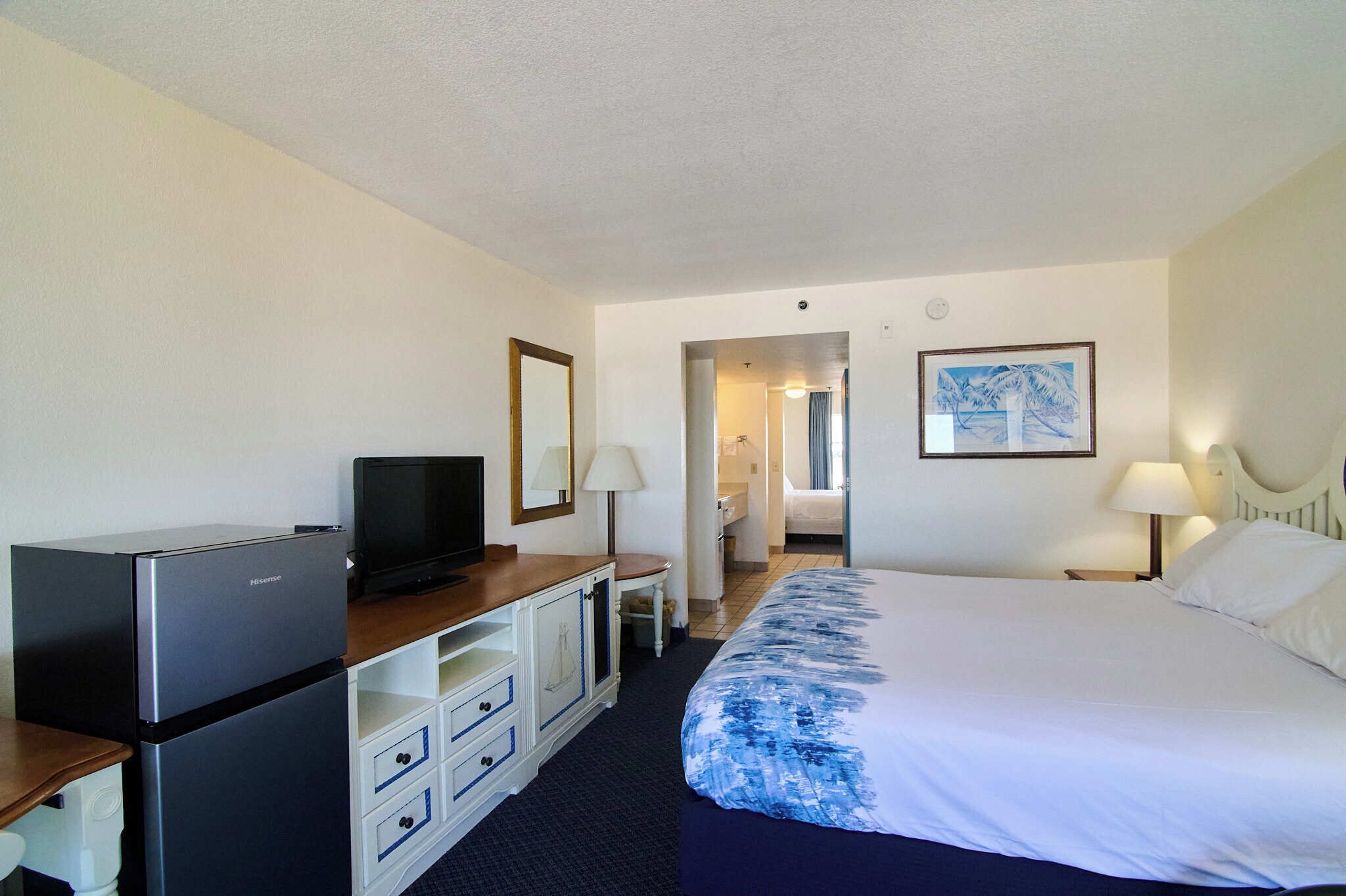 A hotel room with a bed, a TV, a desk, and a bathroom visible through an open door.