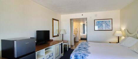 A hotel room with a bed, a TV, a desk, and a bathroom visible through an open door.