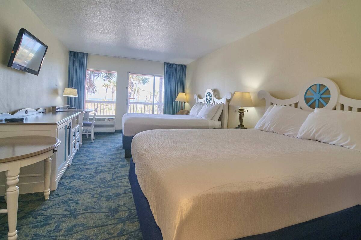 A hotel room with a bed, a desk, a chair, a television, and a window with curtains.