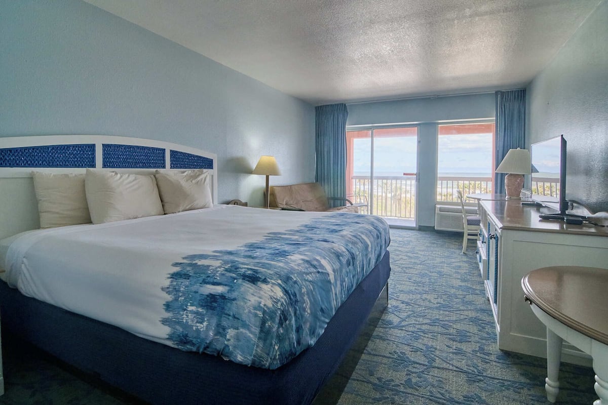 A hotel room with a large bed, a desk, a chair, and a balcony with a view.