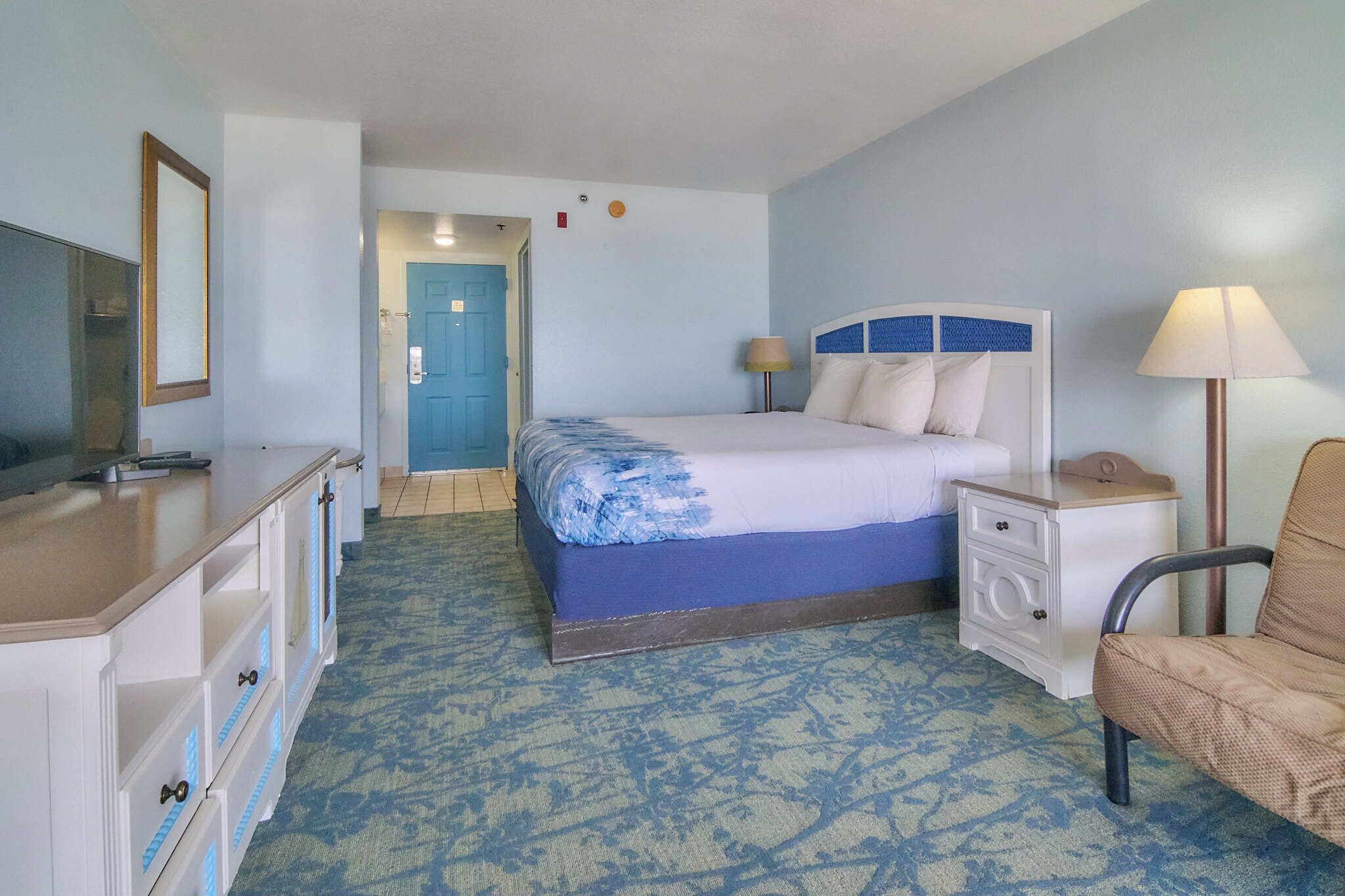 Une chambre d’hôtel comprenant un lit, un bureau, une chaise, une table de chevet, une lampe et un miroir.