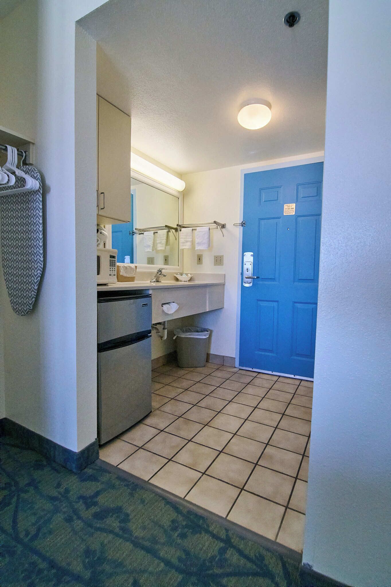 Une petite salle de bain d’hôtel comprenant un lavabo, un miroir et une porte bleue.