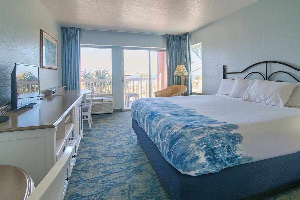 A hotel room with a bed, a desk, a chair, a TV, and a balcony with a view.
