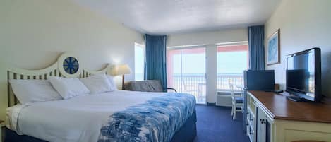 A hotel room with a bed, a desk with a television, a chair, and a view of the ocean.