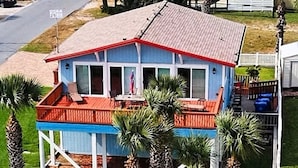 A two-story house with a red roof and blue exterior, featuring a balcony with outdoor furniture.