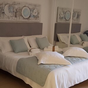 A double bed with a grey headboard, multiple pillows, and a folded white towel.