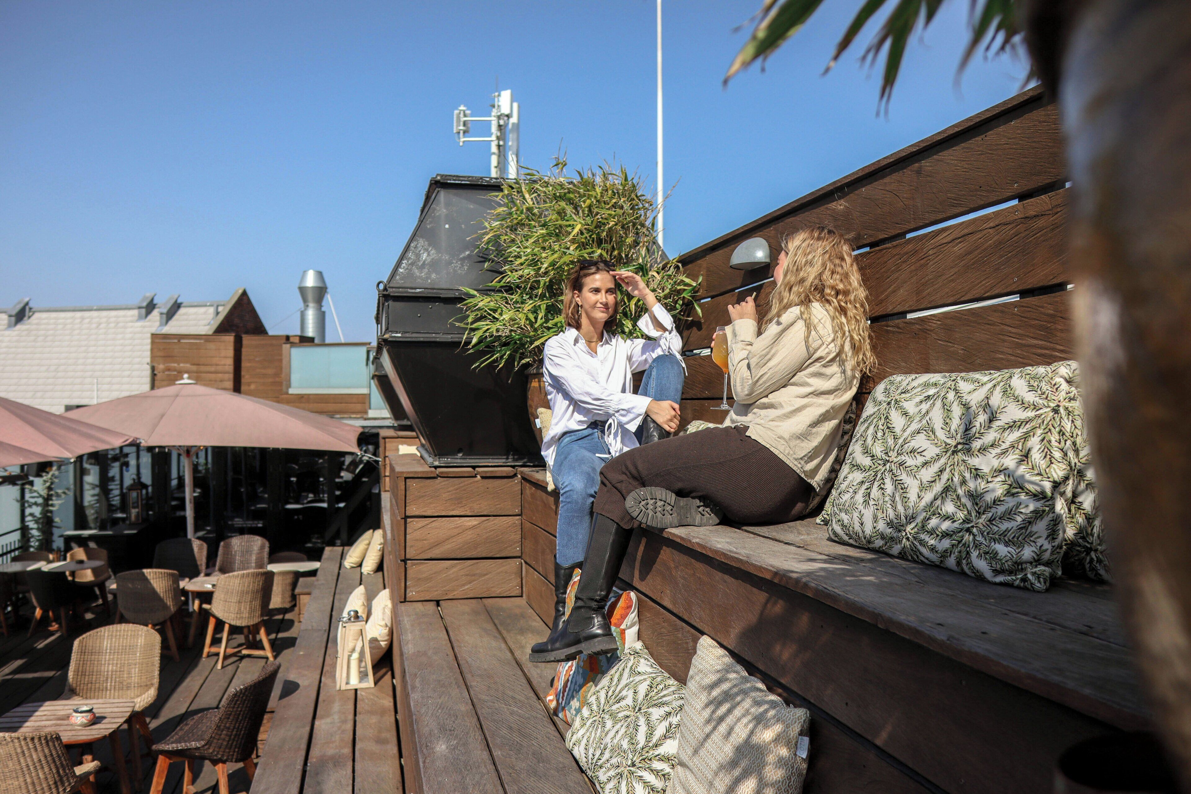 Ein Sitzbereich im Freien mit Holzbänken und Stühlen, einem Grill und Sonnenschirmen.