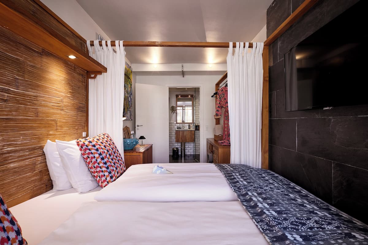 Ein Hotelzimmer mit einem großen Bett, einem Holzkopfteil, einem Flachbildfernseher und einem durchgegangene Tür erkennbaren Badezimmer.