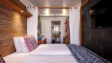 Habitación de hotel con una cama grande, cabecera de madera, televisor de pantalla plana y baño visible a través de una puerta abierta.