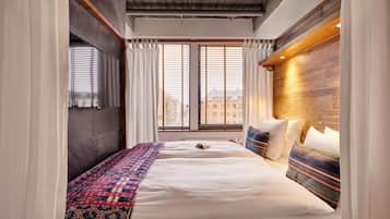 Ett modernt hotellrum med en stor säng, ett träfärgat sänggavel och utsikt över staden genom stora fönster som sträcker sig från golv till tak.