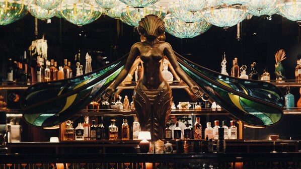 Um bar com uma grande estátua de mulher alada, rodeado por prateleiras de garrafas.