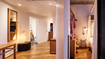 A hotel room with a wooden floor, a bench, a bedside table, a lamp, and a bed with a white curtain.
