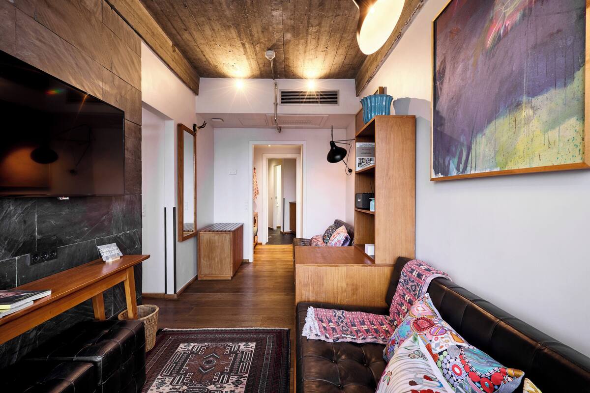 Ein gemütliches Wohnzimmer mit Holzboden, einem schwarzen Ledersofa, einem Holztisch und einem farbenfrohen Teppich.