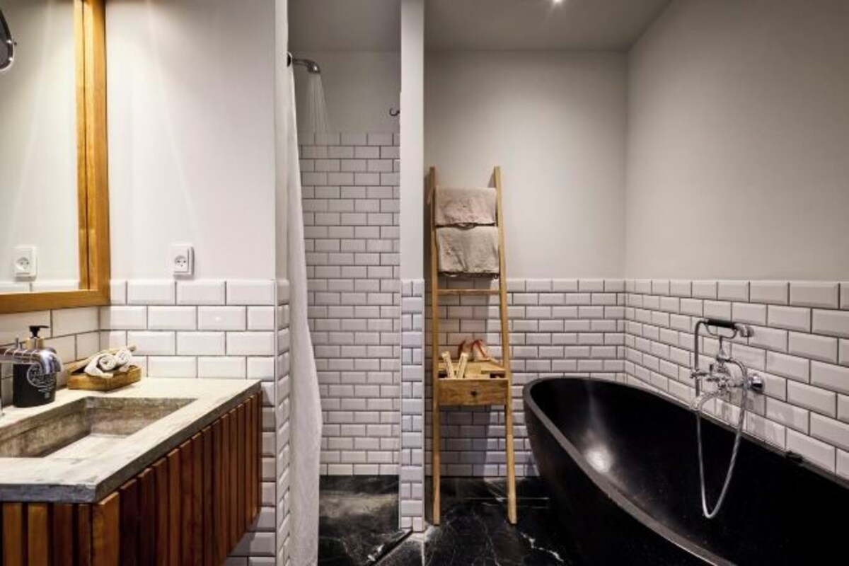 Un baño con tocador de madera, una bañera negra y un perchero para toallas.
