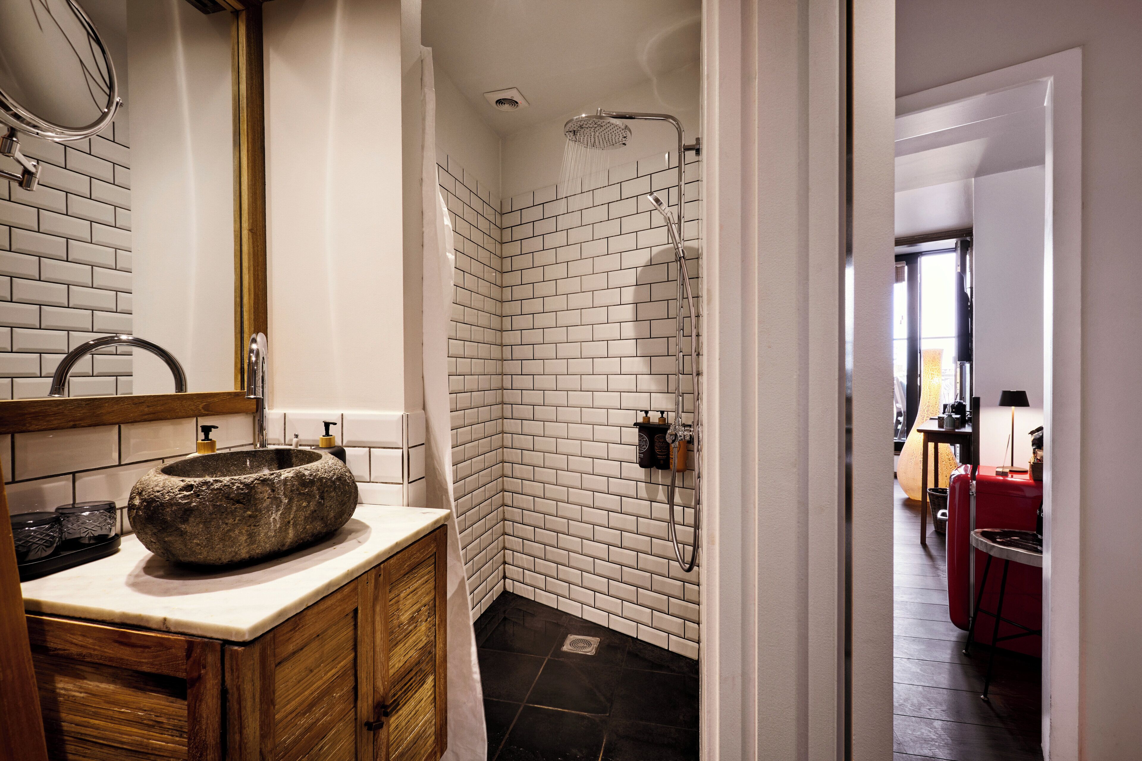 A bathroom with a stone sink, white tiled walls, a shower, and a wooden cabinet.