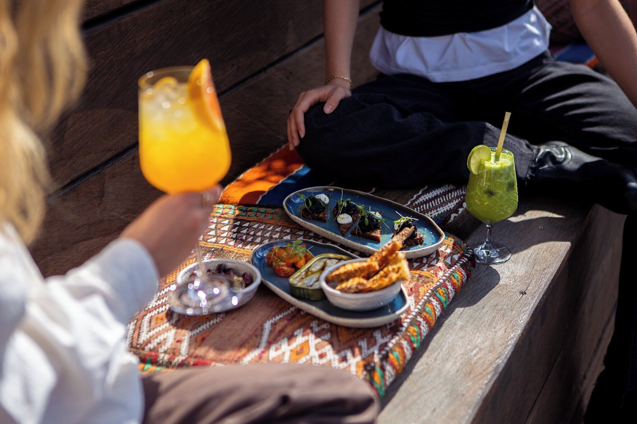 A picnic setup with various dishes and drinks on a wooden bench.