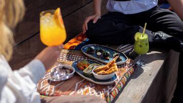 A picnic setup with various dishes and drinks on a wooden bench.