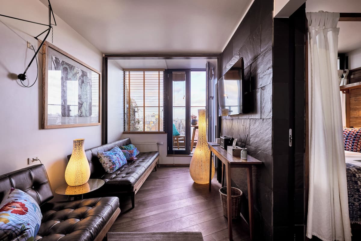 Un salon moderne avec un canapé en cuir, deux lampadaires, un grand tableau et une vue à travers une porte vitrée.