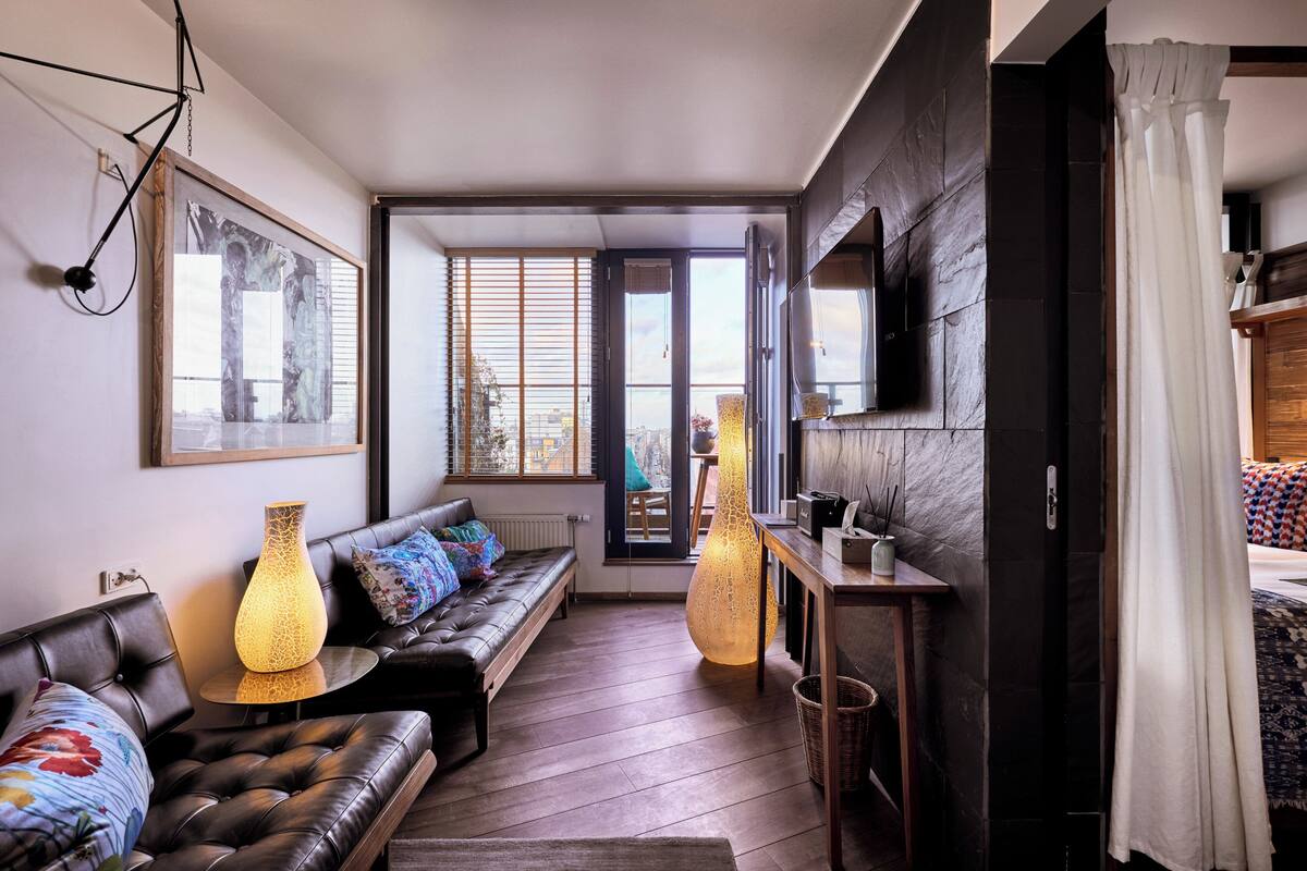 A modern living room with a leather sofa, two floor lamps, a large painting, and a view through a glass door.