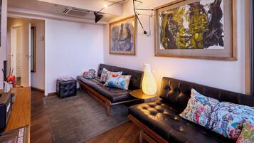 A modern living room with a sofa, a coffee table, and a rug. There are framed artworks on the wall and a door leading to another room.