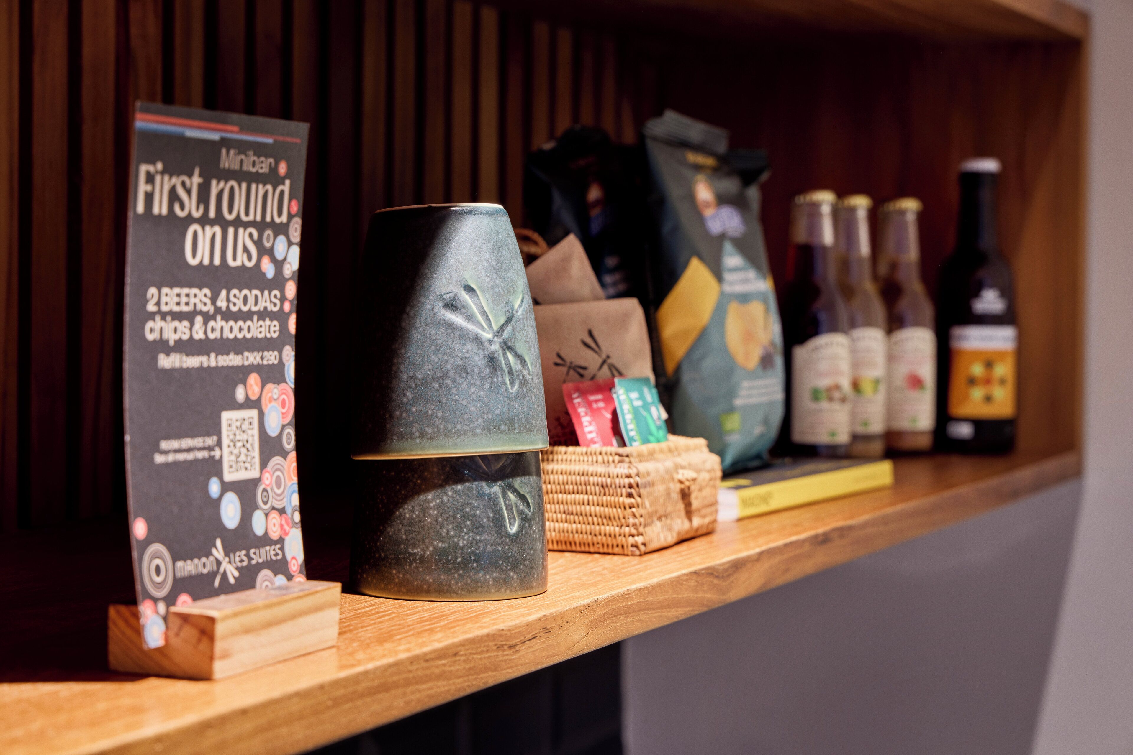 A wooden shelf with a sign for Miniban's First round on us, a ceramic mug, and various packaged goods.