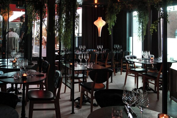 A restaurant interior with tables set for dining, chairs, and hanging plants.