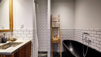 A modern bathroom with a black bathtub, white tiled walls, a wooden ladder, and a wooden vanity with a sink and towel rack.