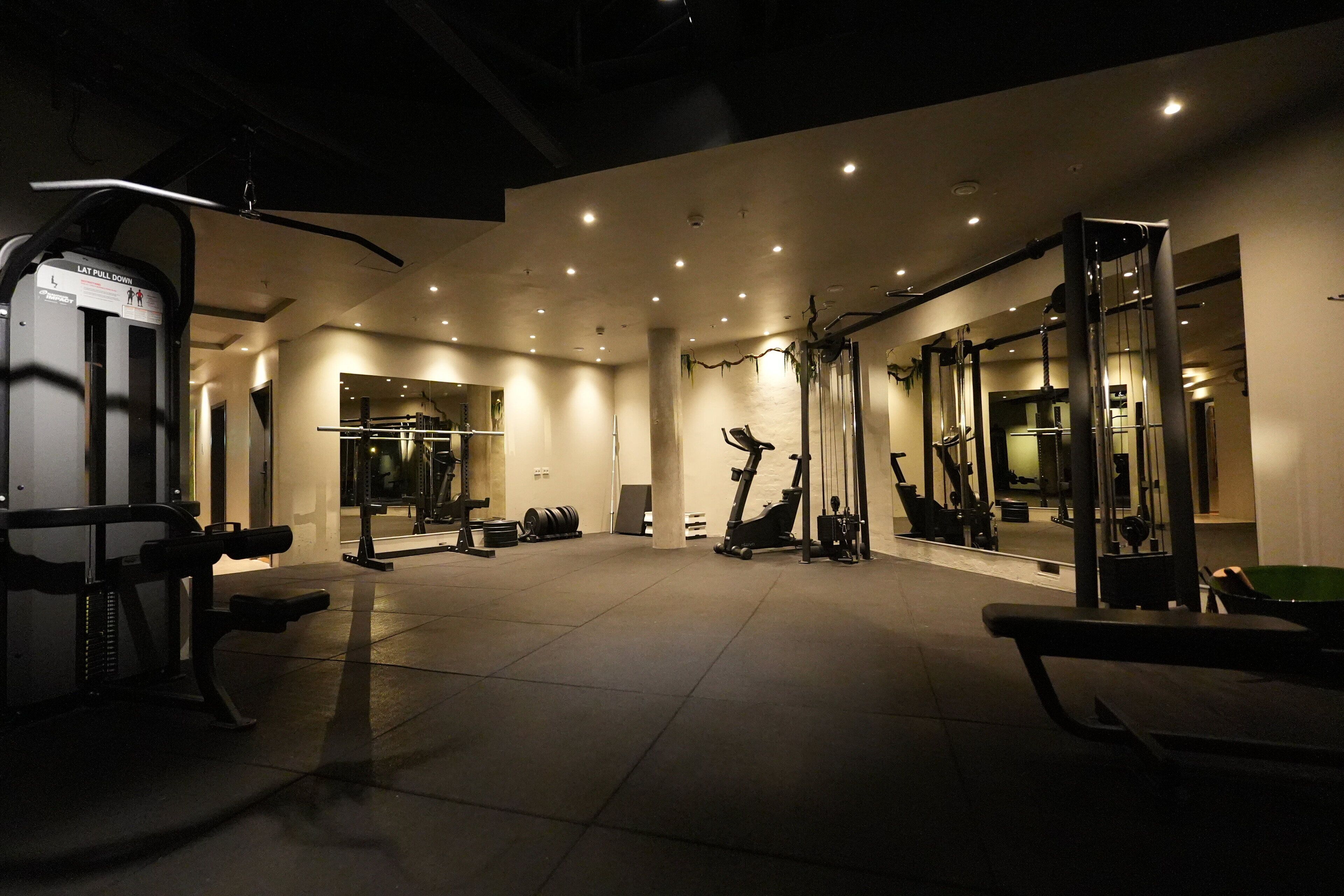 Una palestra con diverse attrezzature per l'esercizio fisico, tra cui un tapis roulant, macchinari per pesi e uno specchio a parete.