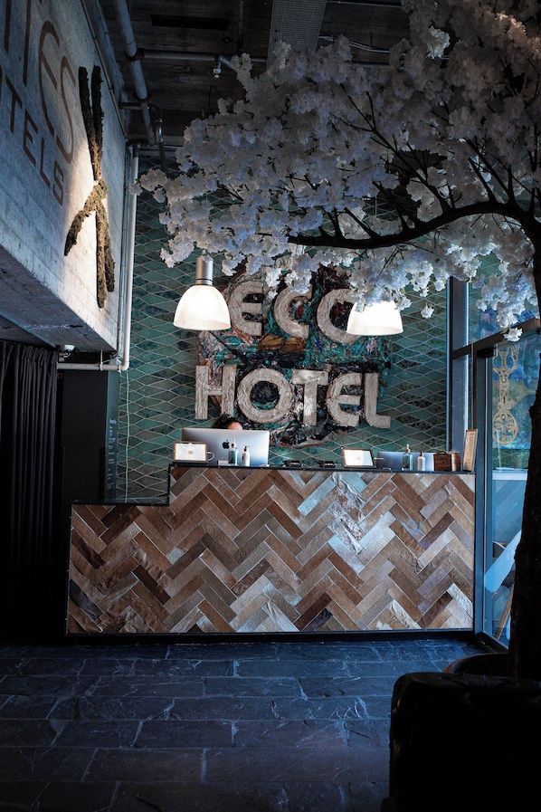 Ein Empfangsschalter mit einem Fischgrätmuster aus Holz, ein großes 'HOTEL'-Schild und eine hängende Blumenkomposition.