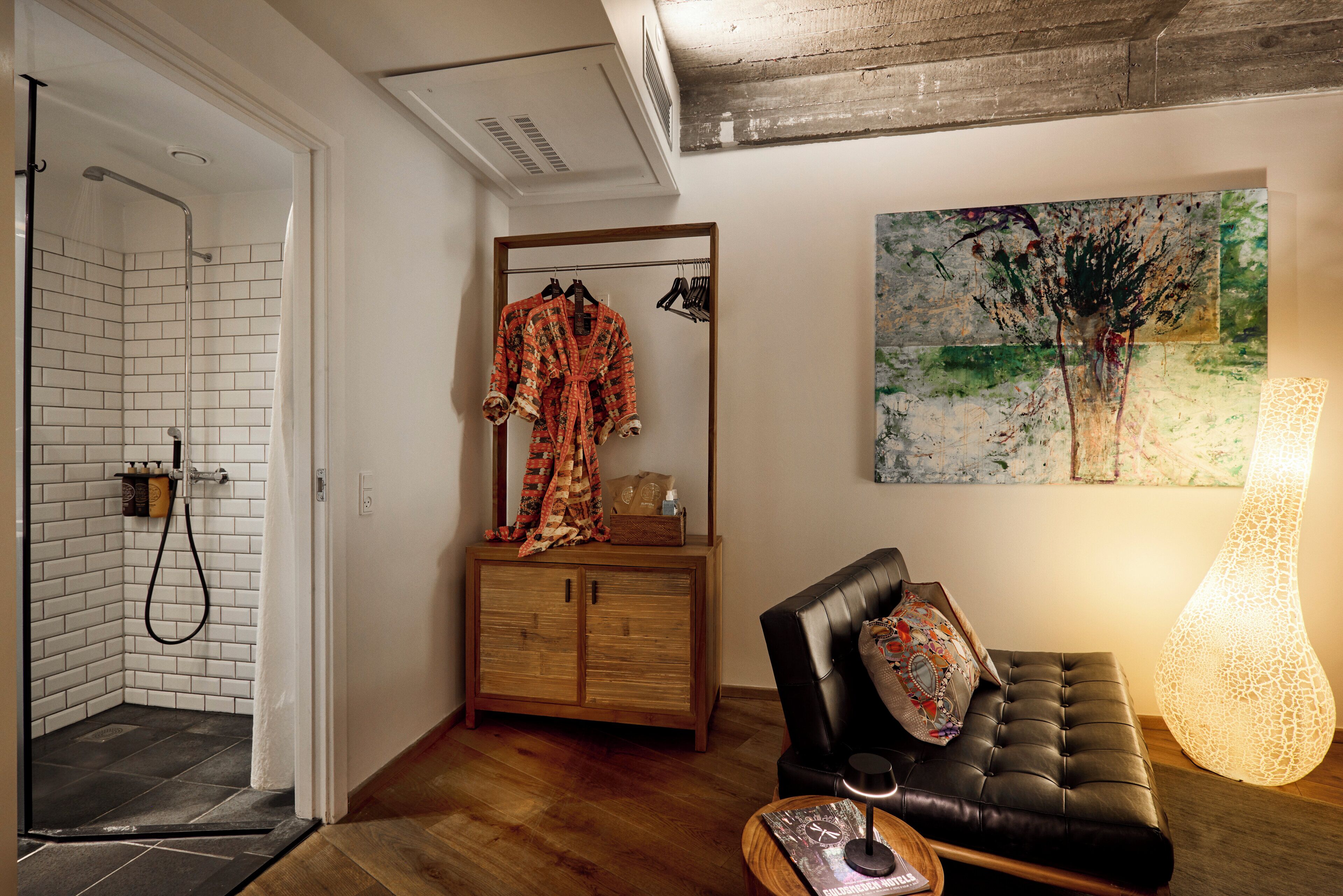 A modern bathroom with a shower, a wooden cabinet with a robe, and a large painting on the wall.
