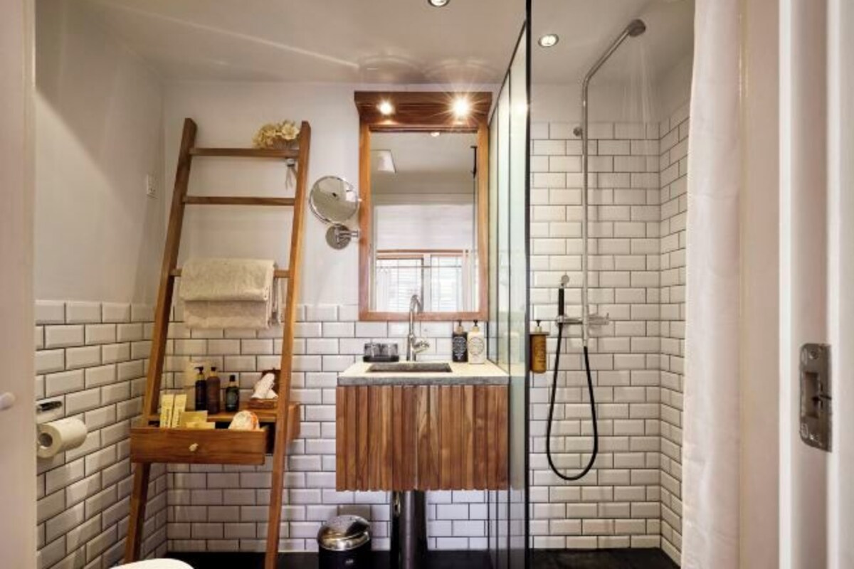 Un baño con una escalera de madera, un lavamanos con espejo, una ducha y una pared de azulejos.