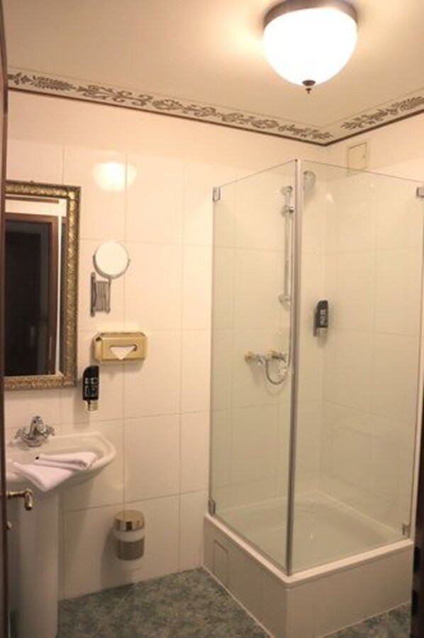 Un baño con ducha compartimentada con vidrio, un lavamanos y un espejo.