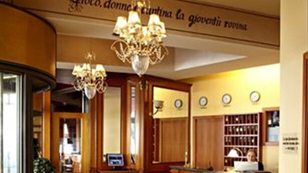 Een hotel lobby met een kroonluchter, een receptiebalie en een betegeld gebied met fauteuils.