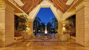 A spacious lobby with a high ceiling, palm trees, and a central seating area.