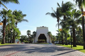 A paved pathway leading to a large, symmetrical building with an archway, surrounded by palm trees and a clear sky. - Bahia Principe Explore Coba - Hyatt Inclusive Collection - All Inclusive (Akumal)