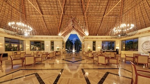 A spacious lobby with a high ceiling and a central chandelier, featuring a geometric floor pattern and seating arrangements.