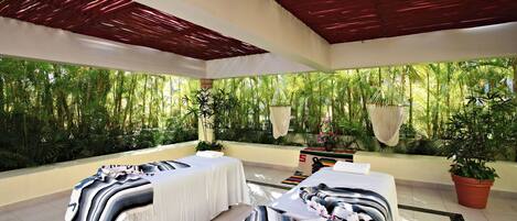 Un cuarto de spa con dos camillas de masaje, un techo con listones rojos y vistas a exuberante follaje exterior.