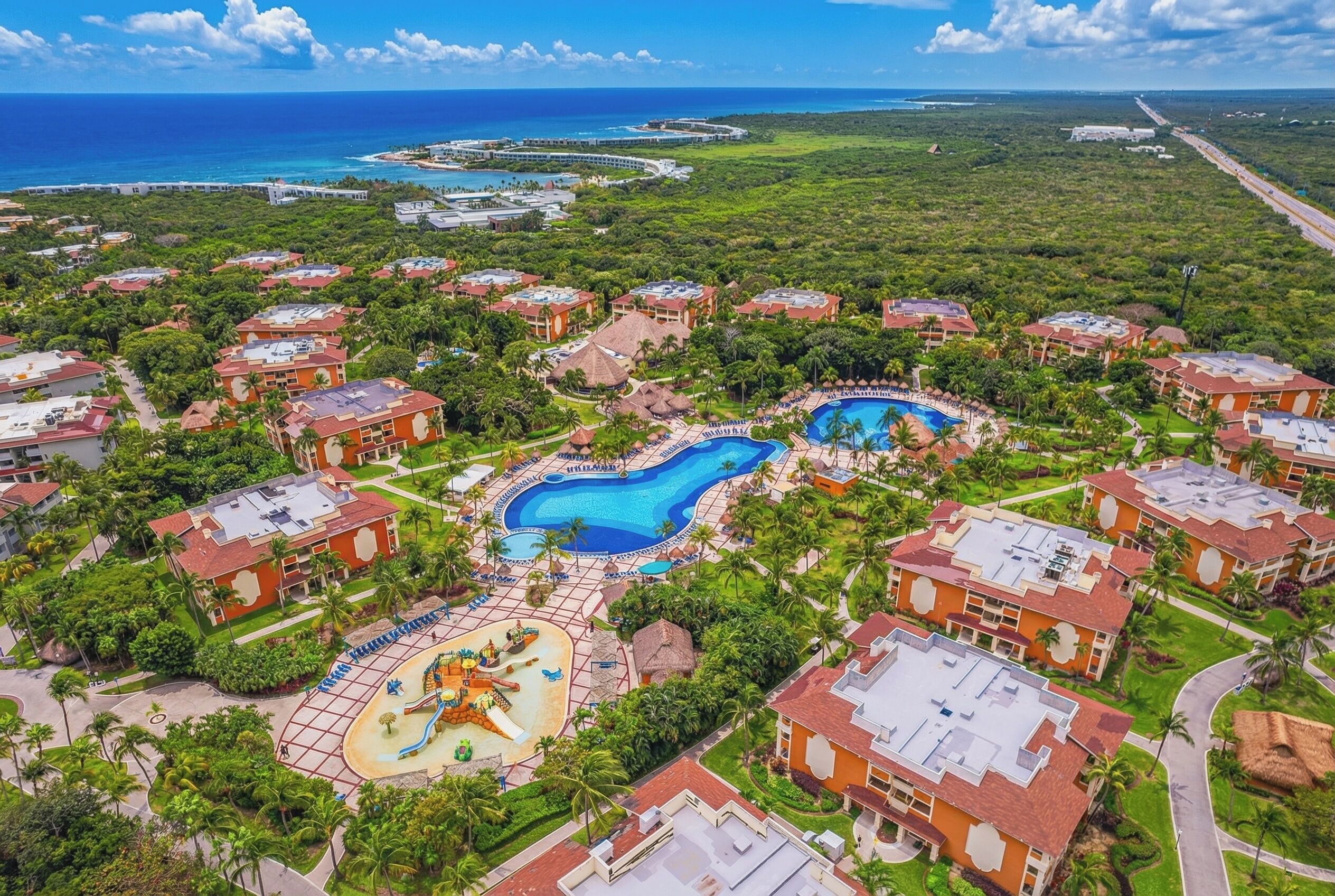 An aerial view of a resort with multiple swimming pools, lush greenery, and beachfront properties.