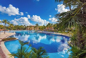A large swimming pool surrounded by palm trees and lounge chairs, with a building in the background. - Bahia Principe Explore Coba - Hyatt Inclusive Collection - All Inclusive (Akumal)