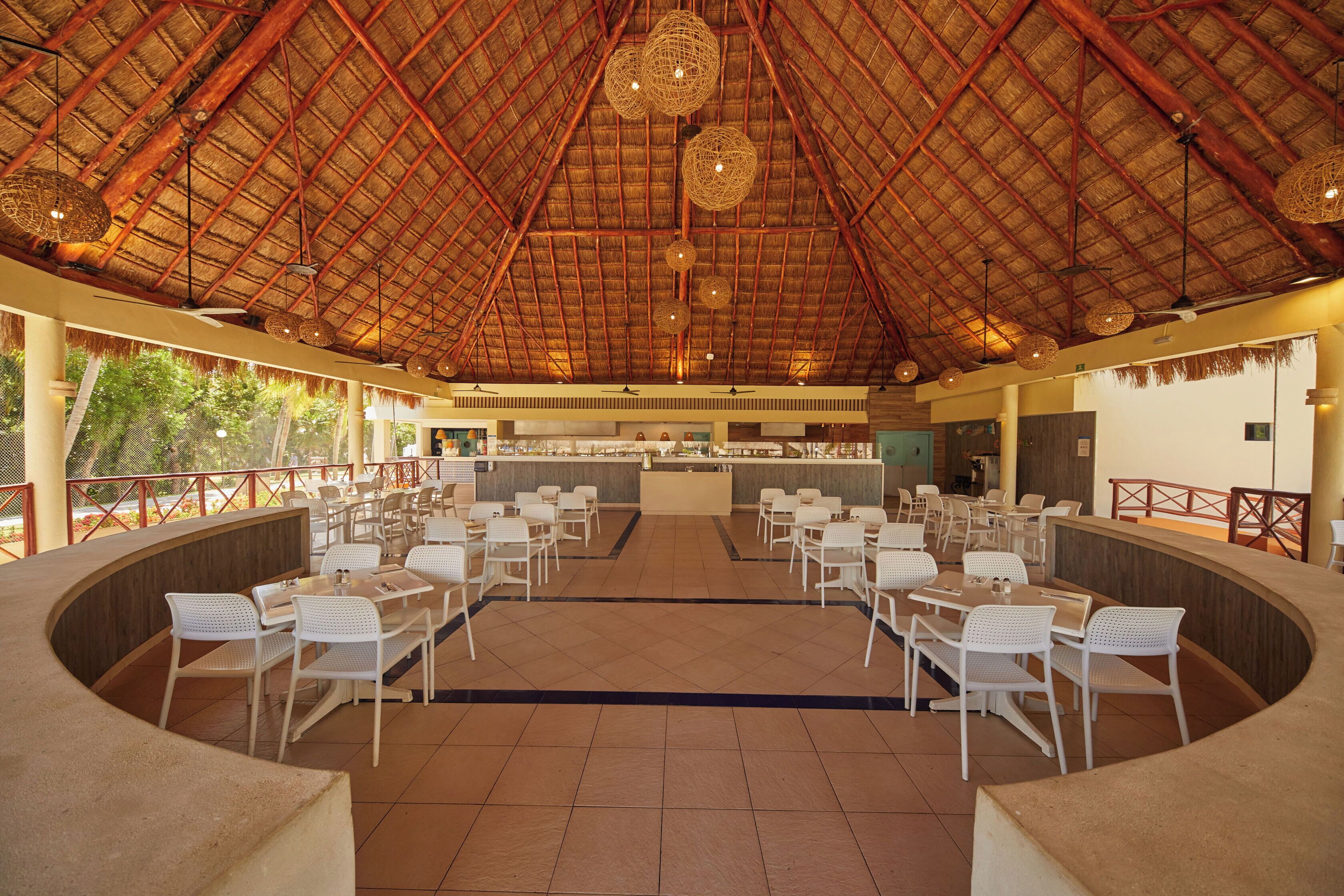 Un comedor interior con techo de paja, sillas blancas y una barra central.